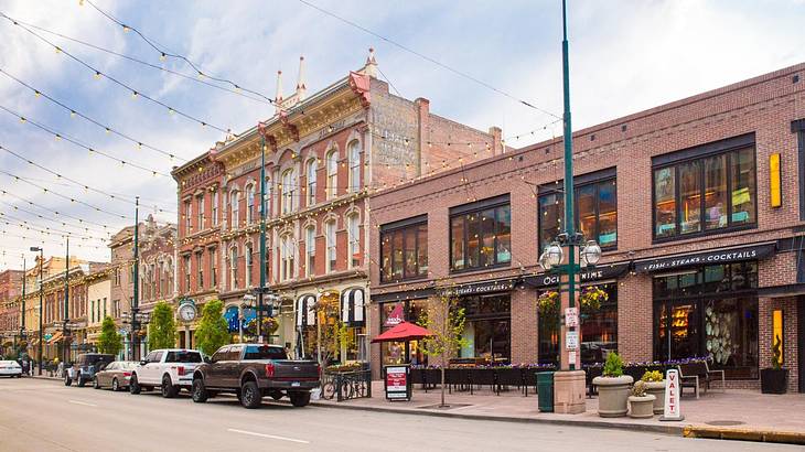 A street with red brick buildings, a patio restaurant, and cars parked on the road