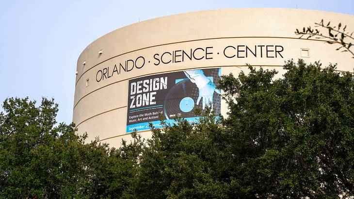 A circular building with a sign on it, surrounded by trees under a cloudy sky