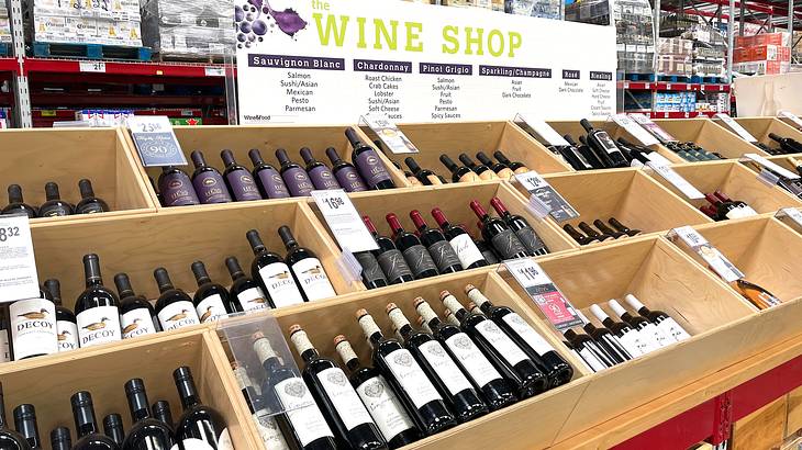 A group of wooden boxes containing bottles of wine lying vertically and a sign above