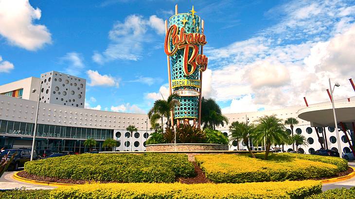 A colorful cylindrical sign on top of green and yellow bushes, with buildings behind