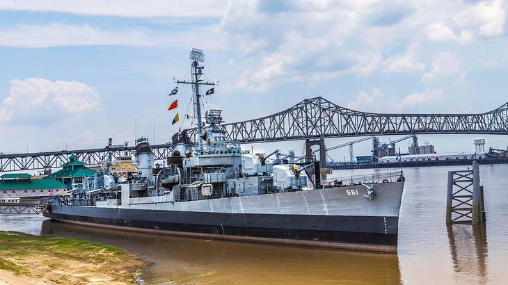 A naval ship on the water with a bridge behind it