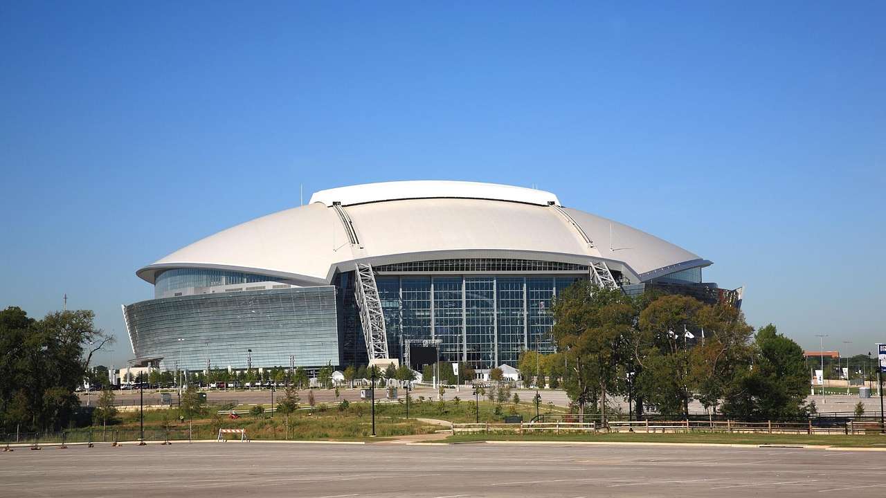 An American football-shaped stadium with a road and trees in front of it