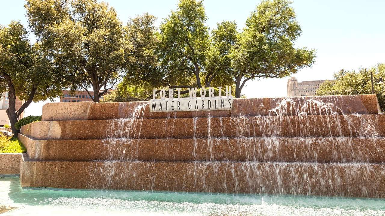 A water fountain flowing into a pool and a sign that says "Fort Worth Water Gardens"