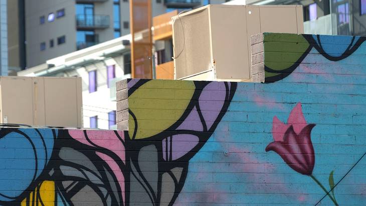 A stepped blue wall with colorful flower graffiti and buildings at the back