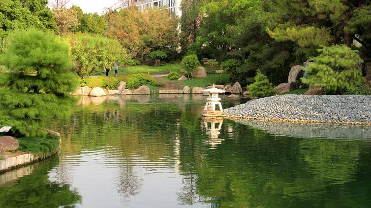 A koi fish pond with a small white Japanese tea house on the edge surrounded by trees