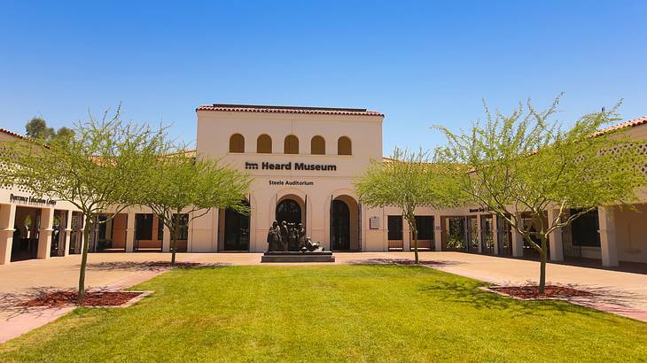 A building with arched doors and windows behind a grassy tree-lined courtyard