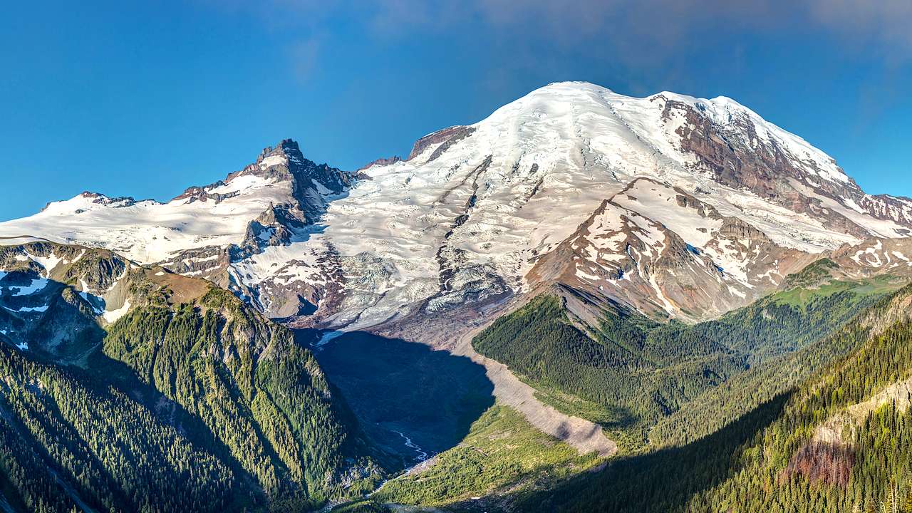 Glacial snow-capped rocky mountain peaks with green vegetation at its base