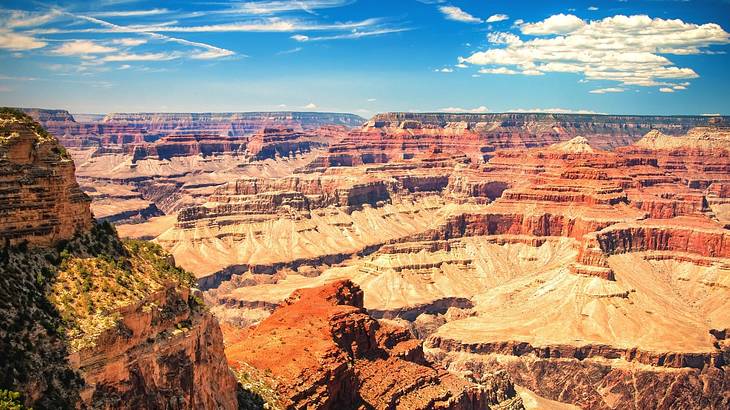 A view across a red rock canyon under a blue sky with clouds