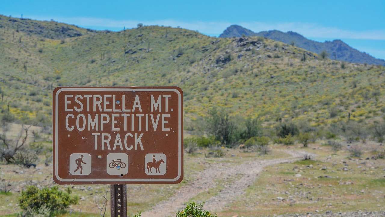 A sign that says "Estrella Mt Competitive Track" in front of green hills