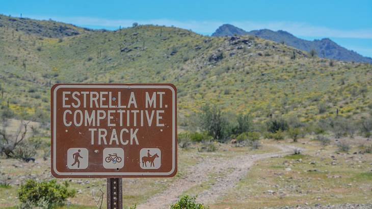 A sign that says "Estrella Mt Competitive Track" in front of green hills