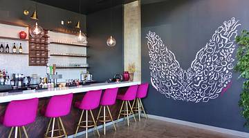 A dining counter with fuchsia chairs and a grey wall with painted white angel wings
