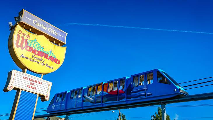 A yellow sign that says "Dutch Wonderland" next to a blue monorail train and blue sky