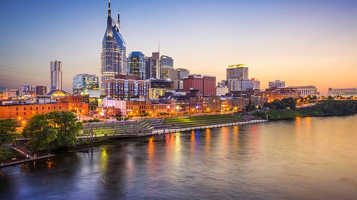 A city skyline at night with a river in front under a dark blue and orange sky