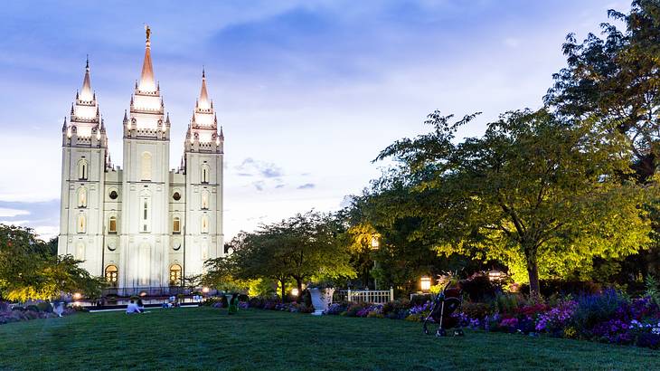 A temple with three towers illuminated in the evening next to a grass lawn with trees