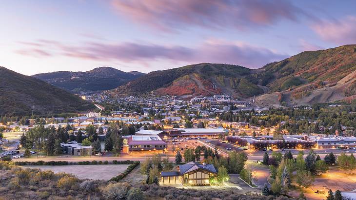 A view of a small town surrounded by greenery-covered hills under a purple sky