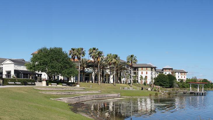 A lake next to green grass, buildings, and palm trees on a clear day