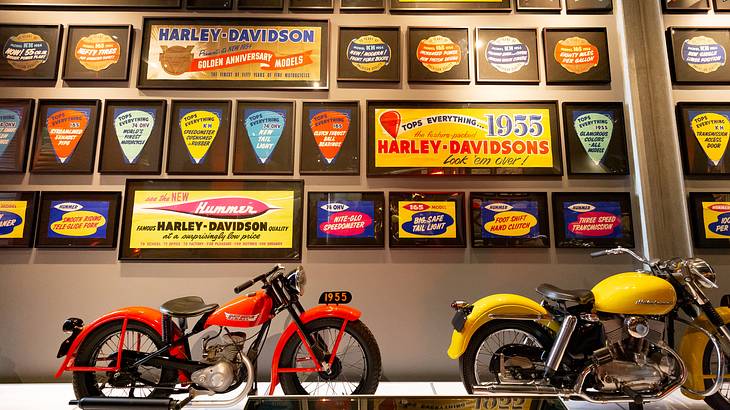 Two motorbikes stand in front of a wall featuring many Harley-Davidson vintage signs