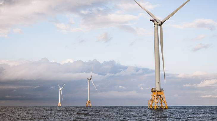 Three large wind turbines rising above the sea against a cloudy, light-blue sky Three large wind turbines rising above the sea against a cloudy, light-blue sky