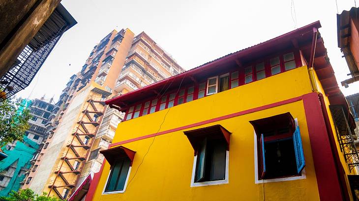 Point of view of a yellow and red heritage house with buildings beside it