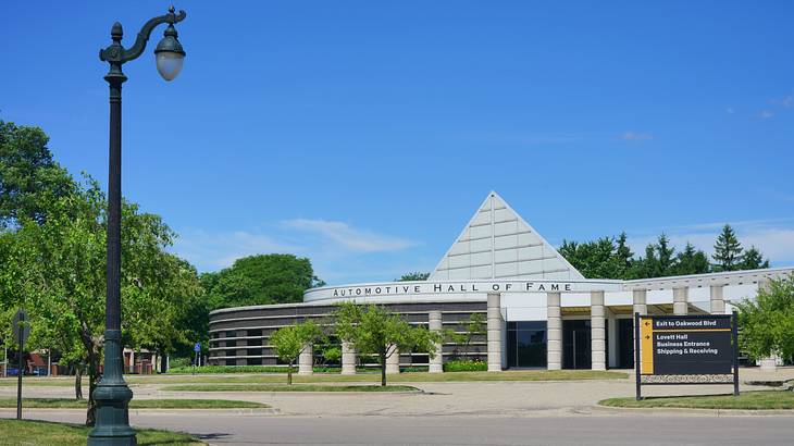 The Facade of a white building with a pyramid atop it next to a paved area and trees