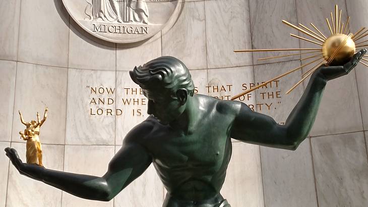 A bronze statue of a man with extended arms carrying a gold sphere in one hand A bronze statue of a man with extended arms carrying a gold sphere in one hand