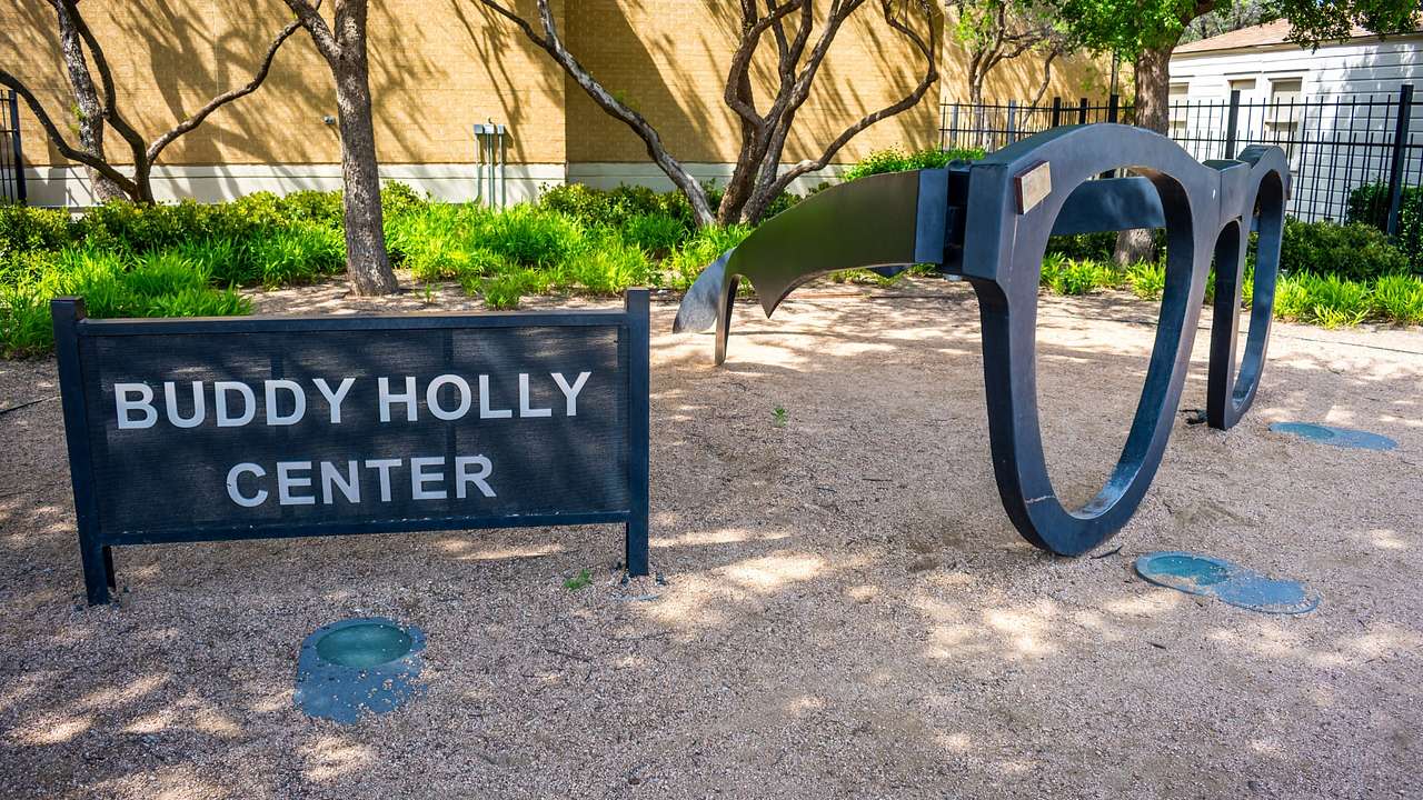 A sign that says "Buddy Holly Center" next to a sculpture of a pair of glasses