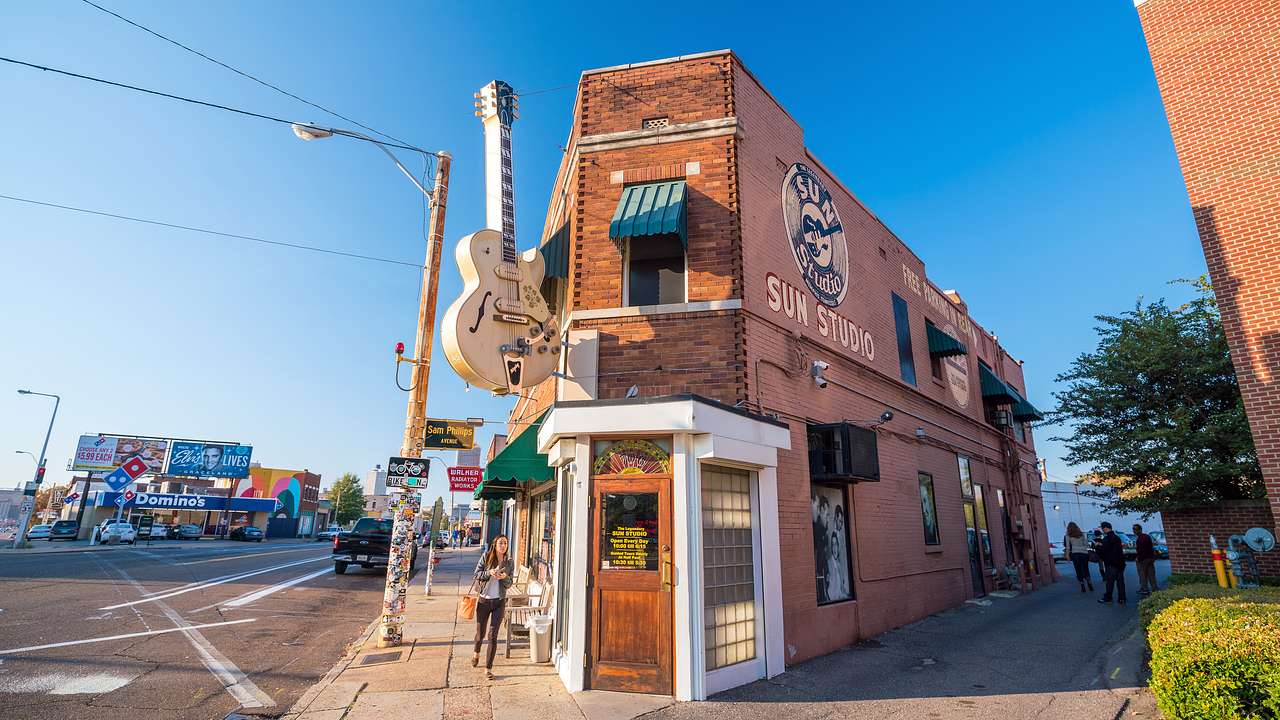 A bricked building with a large guitar sign hanging on the side