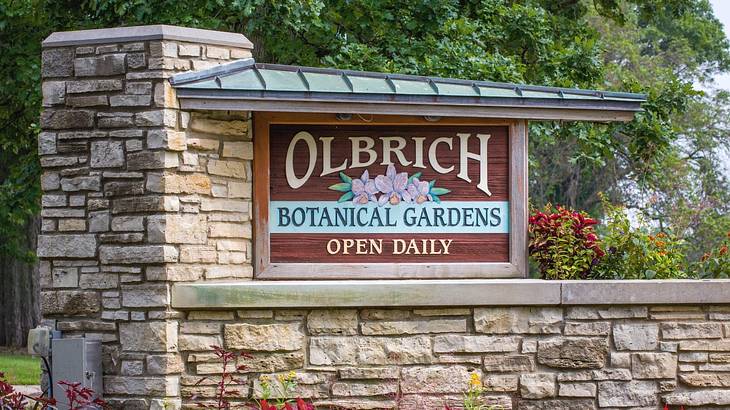 A sign that says "Olbrich Botanical Gardens" with plants around it
