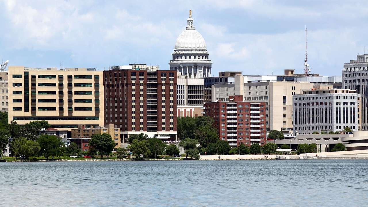 A lake next to city buildings and a stone state capitol building with a domed roof