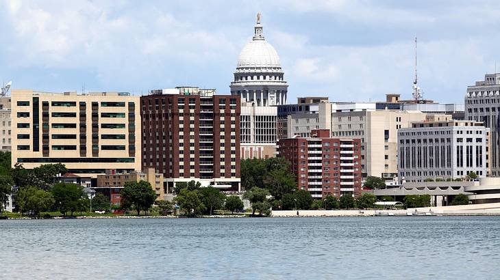 A lake next to city buildings and a stone state capitol building with a domed roof
