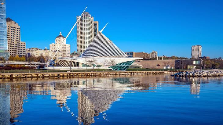 A lake next to a city with tall buildings and a modern structure under a blue sky