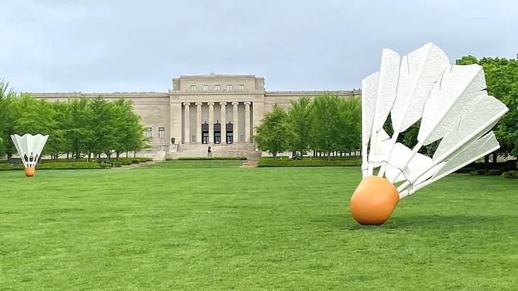 A green lawn with shuttlecock sculptures on it and a stone building in the background