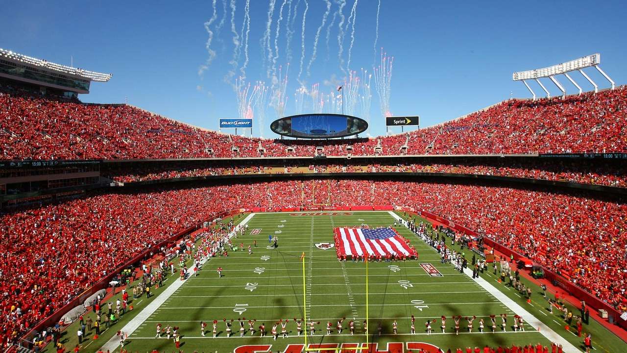 A football field with a US flag and fans wearing red jerseys in the stands