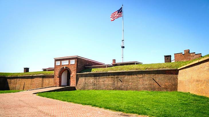 A rectangular fort with a tall flag on top and green grass and a path in front