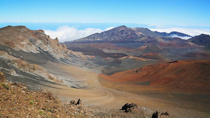 Brown and red volcanic hilly terrain above white clouds and against blue sky