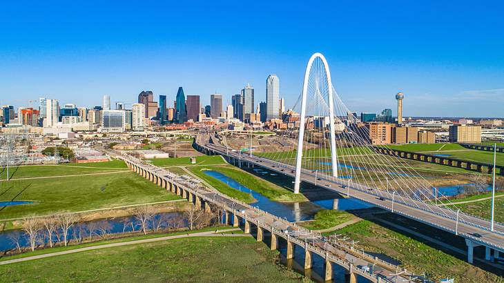 A city skyline and a white bridge next to grass and a waterway