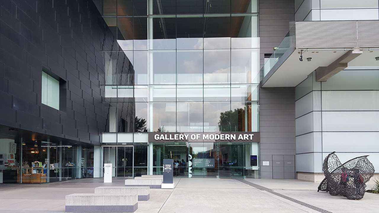 Entrance to a grey building with glass and a board that reads "Gallery of Modern Art"