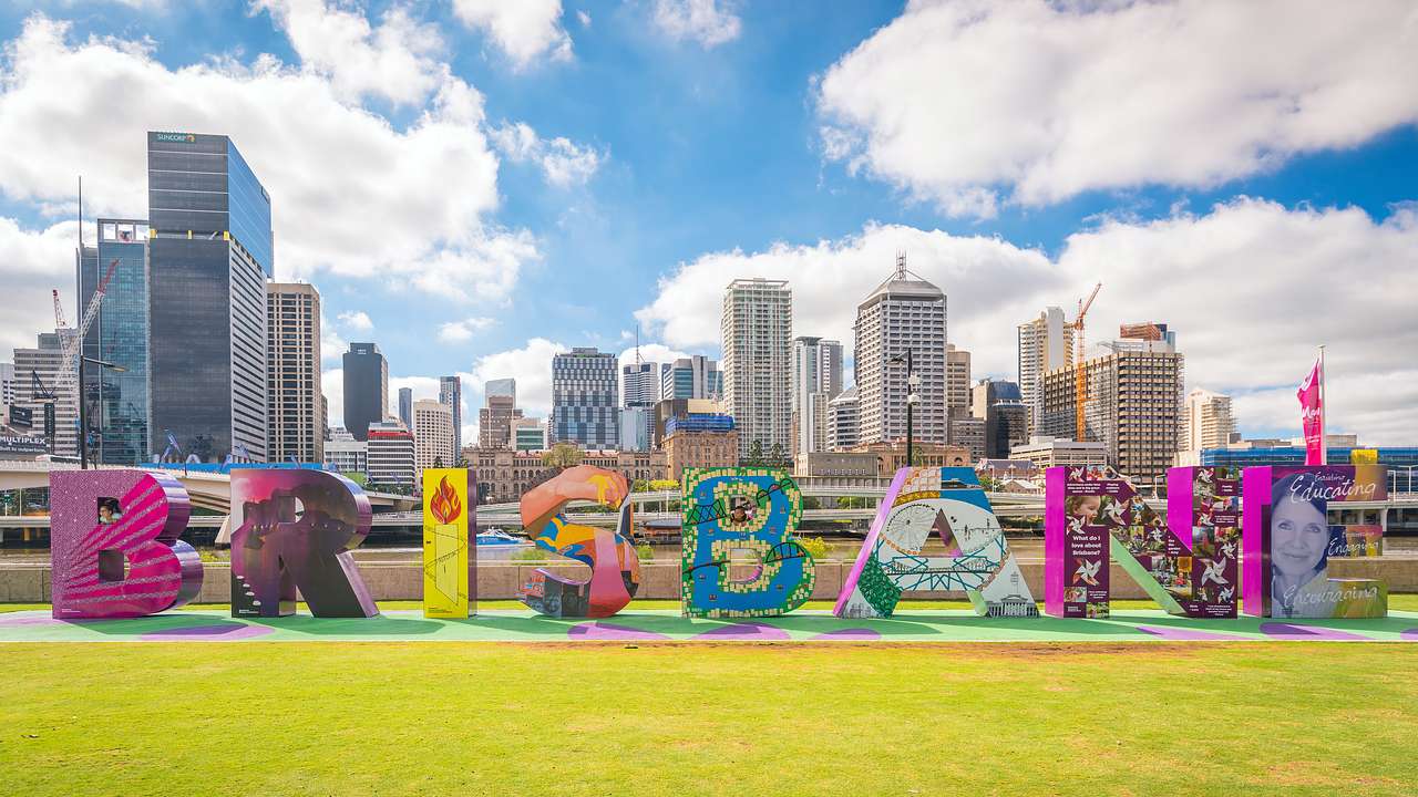 Eight large colourful letter blocks that read "Brisbane," with a city skyline behind