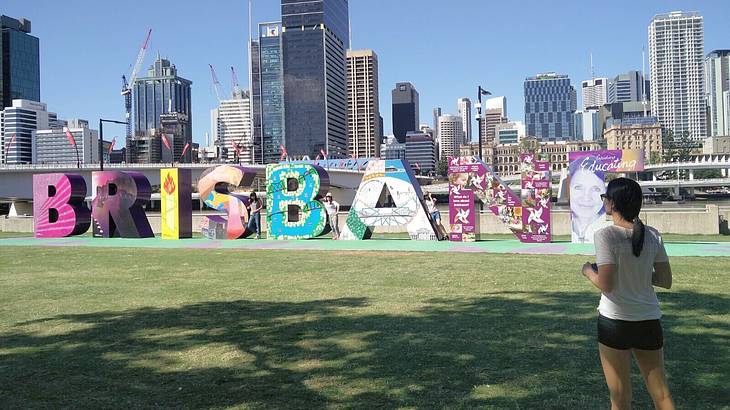Eight large colourful letter blocks that read "Brisbane," with a city skyline behind
