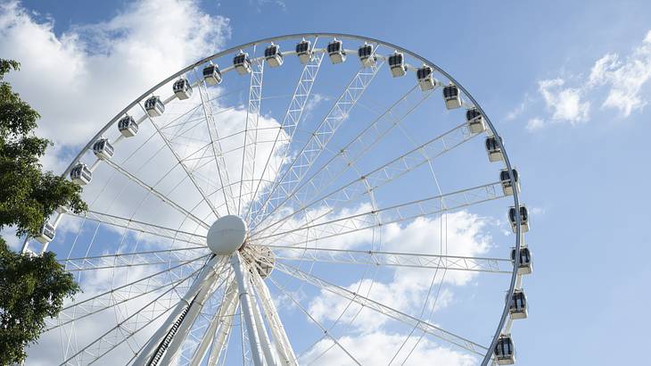A giant wheel with a tree to its left and a blue cloudy sky
