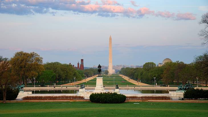 A long mall with green grass and an obelisk in the distance under a blue sky