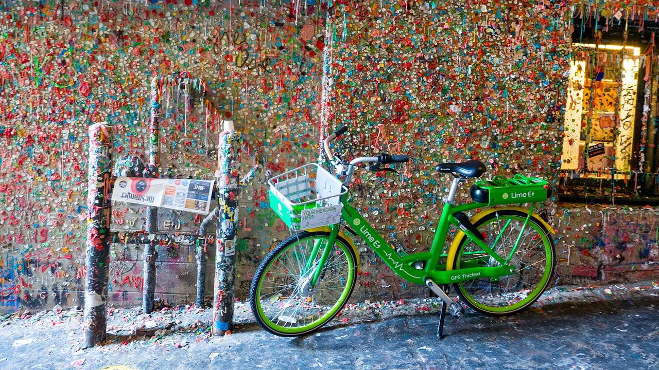 A brick wall covered in colorful chewing gum with a green bike in front of it