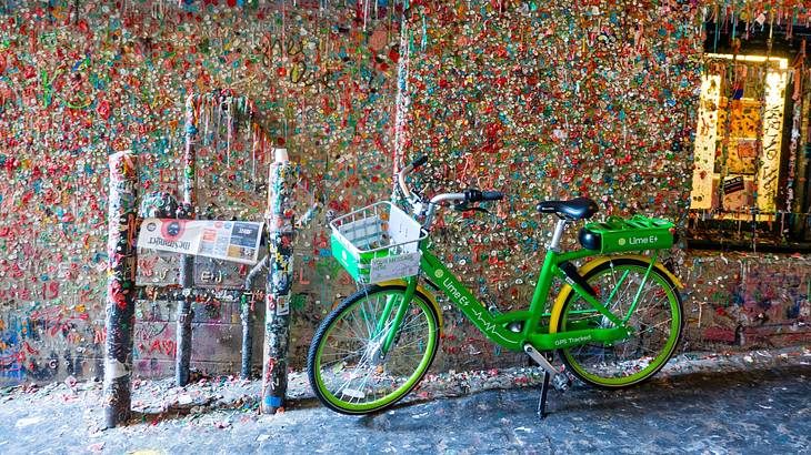 A brick wall covered in colorful chewing gum with a green bike in front of it