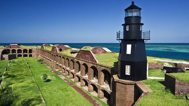A black lighthouse on the brick walls of an old fort next to the ocean