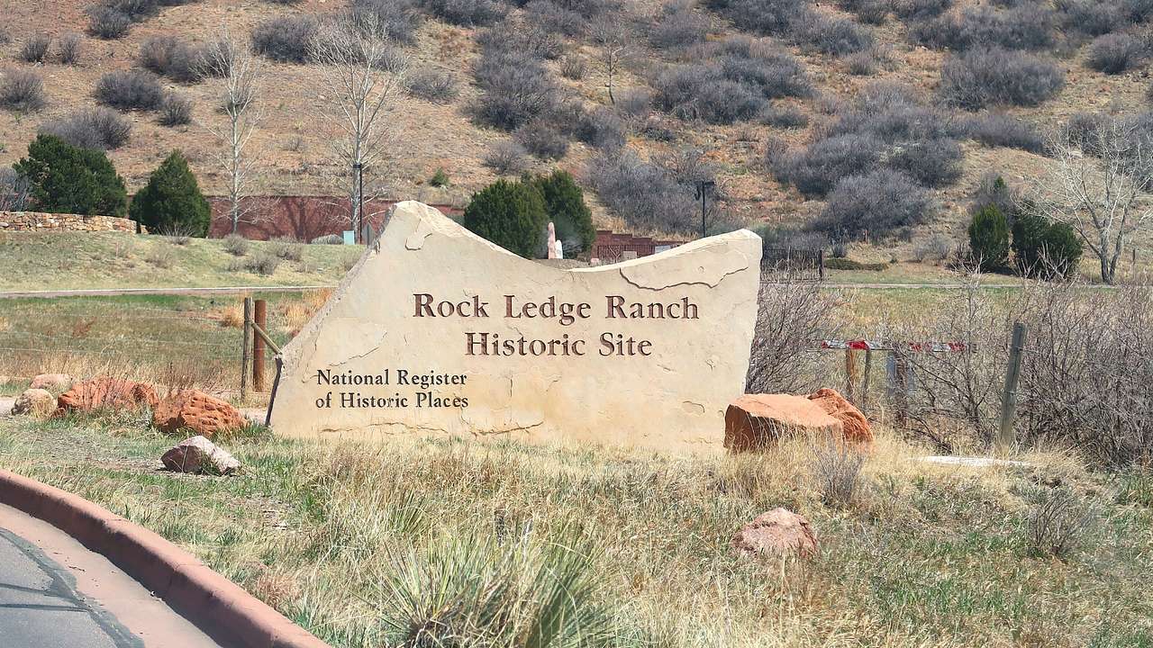 A sign that says "Rock Ledge Ranch Historic Site" surrounded by grass and shrubs