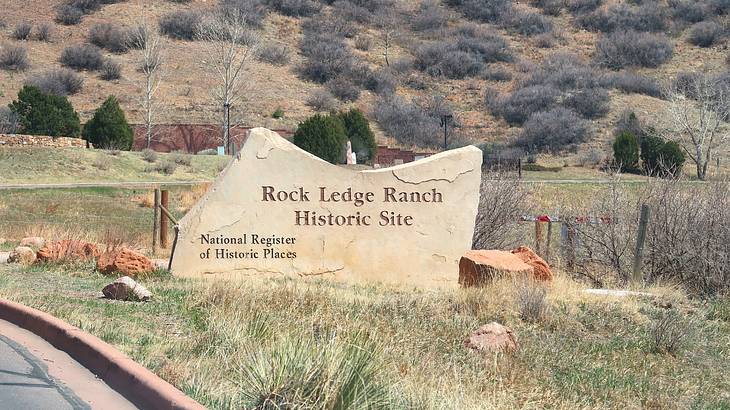 A sign that says "Rock Ledge Ranch Historic Site" surrounded by grass and shrubs