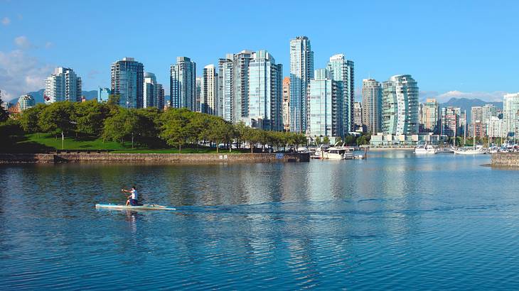 A kayak on the water next to city buildings and trees on a clear day