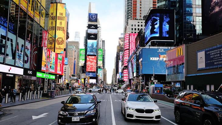 A road with cars surrounded by people walking and buildings with LED screens A road with cars surrounded by people walking and buildings with LED screens
