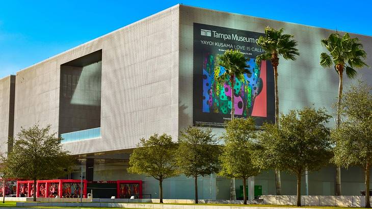 A modern square building with a "Tampa Museum of Art" banner and trees in front