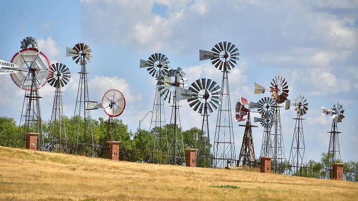Multiple American windmills on the grass under a blue sky with clouds